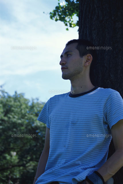 公園で木に寄りかかる若者男性 の写真素材 イラスト素材 アマナイメージズ