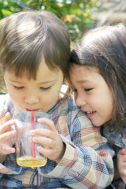 庭でジュースを飲む双子の女の子 a の写真素材 イラスト素材 アマナイメージズ