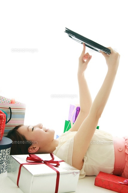 たくさんのギフトと寝ながらタブレットｐｃを操作する女性 の写真素材 イラスト素材 アマナイメージズ