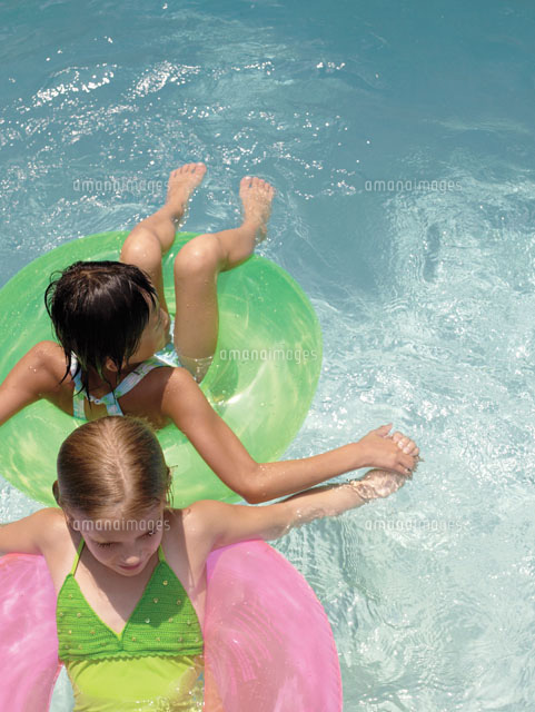 浮き輪でプールに浮かぶ少女2人 の写真素材 イラスト素材 アマナイメージズ