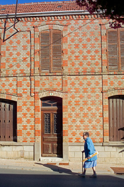 レンガの建物前を歩く老女 の写真素材 イラスト素材 アマナイメージズ