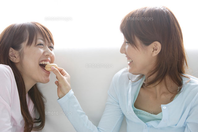 ソファでお菓子を食べる女性2人 の写真素材 イラスト素材 アマナイメージズ