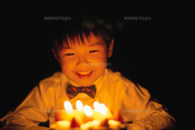 ケーキに立てられたろうそくの炎に照らされる日本人の男の子 の写真素材 イラスト素材 アマナイメージズ