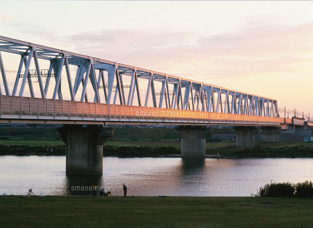 夕陽に輝く鉄橋と河原で憩う人 の写真素材 イラスト素材 アマナイメージズ