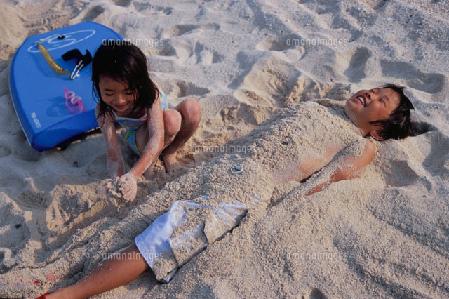 男の子を砂に埋める女の子 の写真素材 イラスト素材 アマナイメージズ