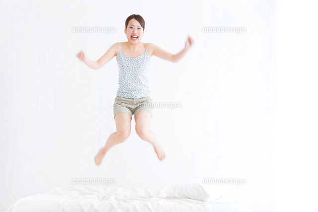 ベッドでジャンプしている女性 の写真素材 イラスト素材 アマナイメージズ