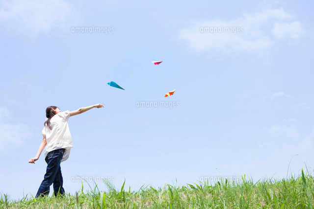 青空の下で紙飛行機を飛ばしている女性 の写真素材 イラスト素材 アマナイメージズ