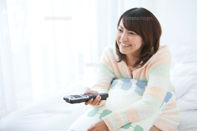 ベッドに座ってテレビを見ている女性 の写真素材 イラスト素材 アマナイメージズ