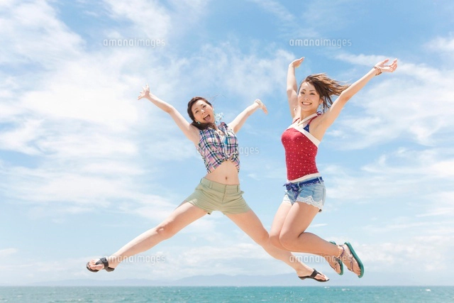 海辺でジャンプする笑顔の女性2人[07800025147]の写真・イラスト素材