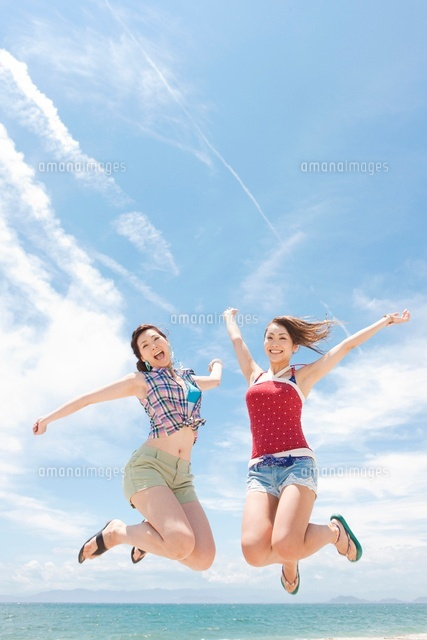 海辺でジャンプする笑顔の女性2人[07800025147]の写真・イラスト素材