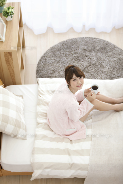 ベッドでマグカップを持つ女性 の写真素材 イラスト素材 アマナイメージズ