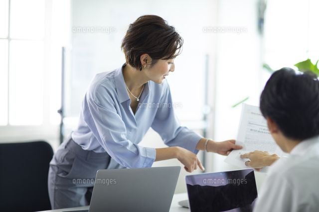 同僚に資料を渡す女性 の写真素材 イラスト素材 アマナイメージズ