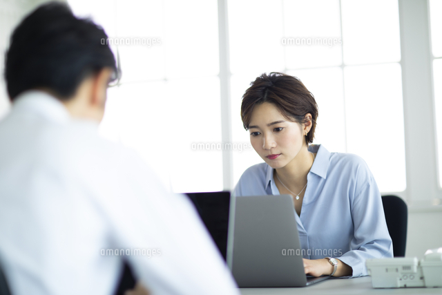 向かい合わせのデスクで仕事する男女 の写真素材 イラスト素材 アマナイメージズ