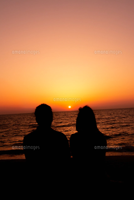 沈む夕日とカップルのシルエット[10112002934]の写真・イラスト素材
