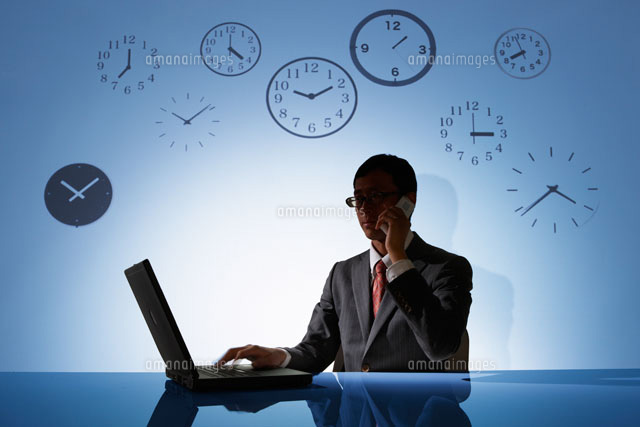 時計の背景の前でパソコンで仕事をするビジネスマン の写真素材 イラスト素材 アマナイメージズ