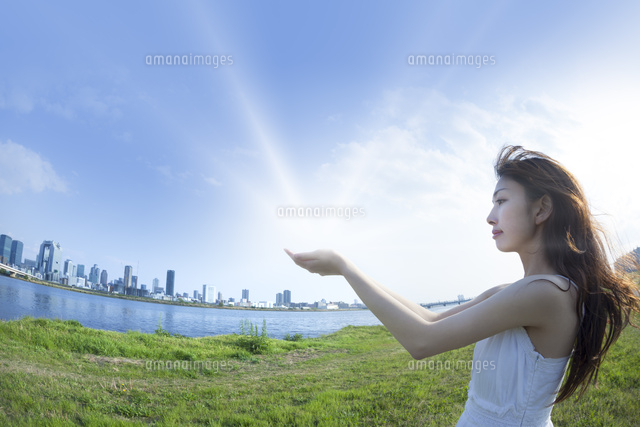 都会の青空の下で手から光を放つ女性 の写真素材 イラスト素材 アマナイメージズ