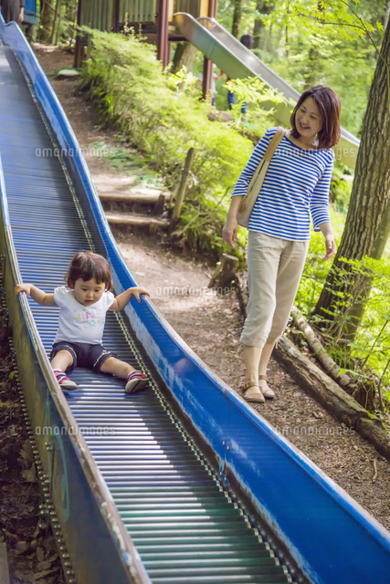 滑り台で遊ぶ子供を見つめる母親 の写真素材 イラスト素材 アマナイメージズ