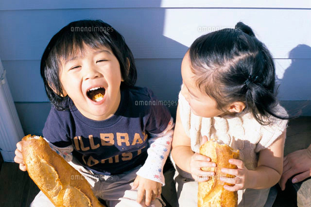 フランスパンを食べる子供をひざに乗せたお母さん[10161006452]の写真