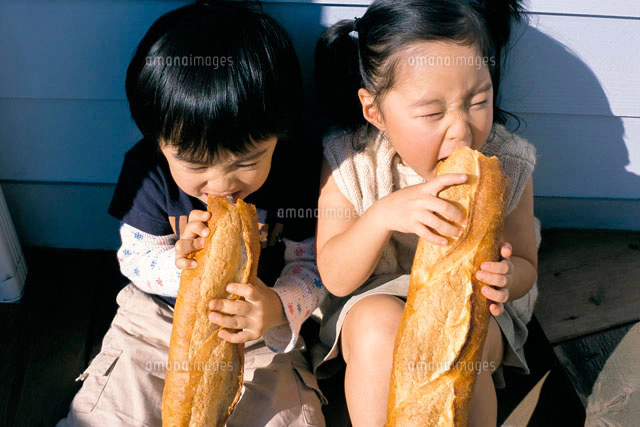 フランスパンを食べる子供をひざに乗せたお母さん 横向き[10161006459