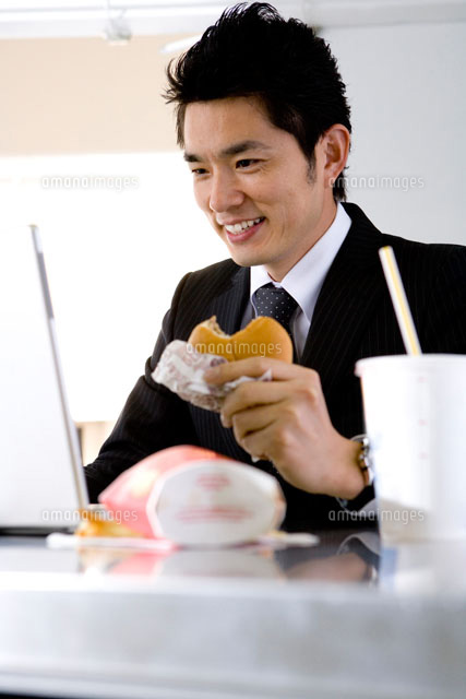 ハンバーガーを食べながら仕事をするサラリーマン の写真素材 イラスト素材 アマナイメージズ