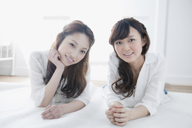 絨毯に寝転がり見つめる女子大生二人[10161009120]の写真・イラスト 