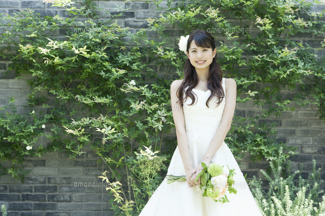 ウェディングドレス姿でブーケを持ち中庭に立つ若い女性 の写真素材 イラスト素材 アマナイメージズ