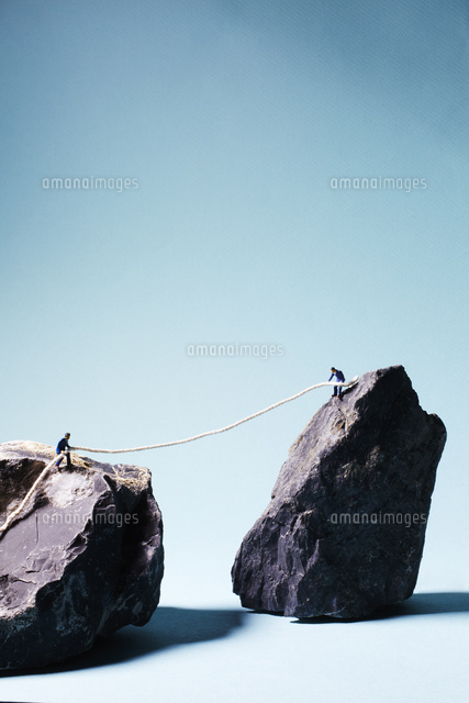 2つの岩山の上でロープを引き合う男性 の写真素材 イラスト素材 アマナイメージズ