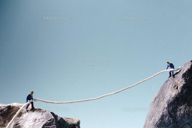 2つの岩山の上でロープを引き合う男性 の写真素材 イラスト素材 アマナイメージズ