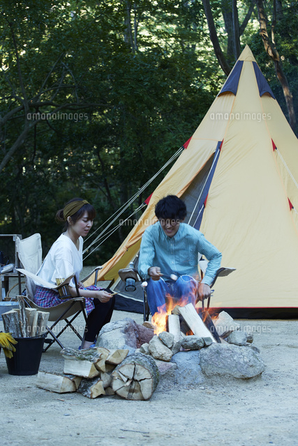 たき火を囲ってマシュマロを食べる男女 の写真素材 イラスト素材 アマナイメージズ