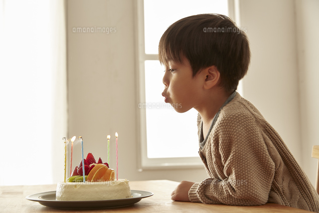 お祝いのケーキのろうそくの火を吹き消している男の子 の写真素材 イラスト素材 アマナイメージズ