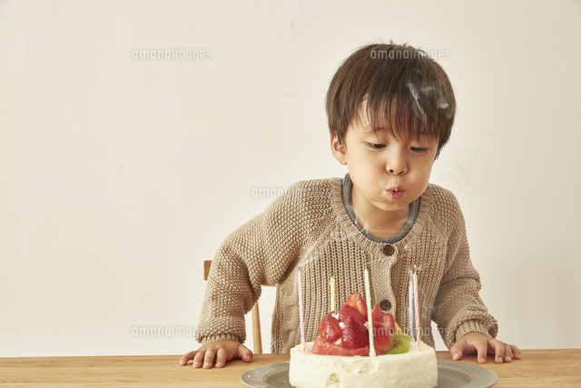お祝いのケーキのろうそくの火を吹き消している男の子 の写真素材 イラスト素材 アマナイメージズ