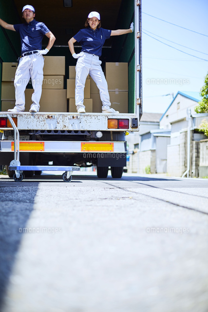 路上でトラックの荷台に載ってポーズをとる作業着の男女[10179015020 