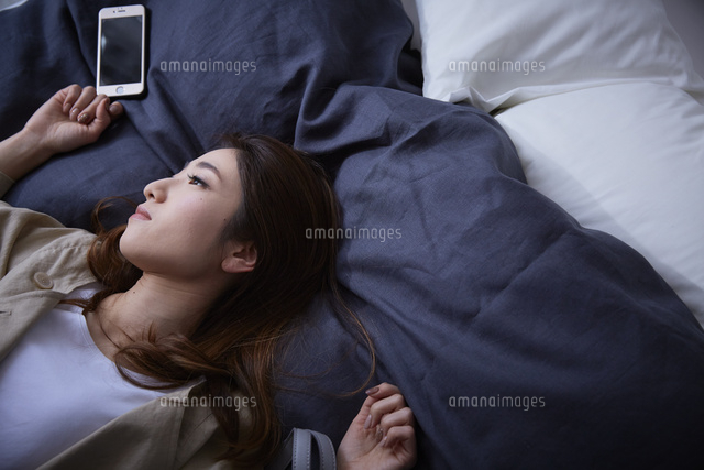ネイビーのカバーのベットに倒れこむ暗い表情の女性 の写真素材 イラスト素材 アマナイメージズ