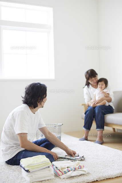 ソファーに座って赤ちゃんをあやす母と洗濯物をたたむ父 の写真素材 イラスト素材 アマナイメージズ