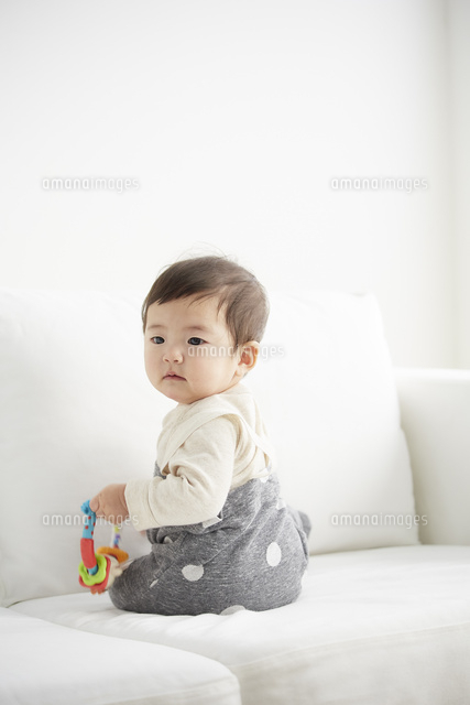 白いソファの上でおもちゃを持ちながら振り向く赤ちゃん の写真素材 イラスト素材 アマナイメージズ
