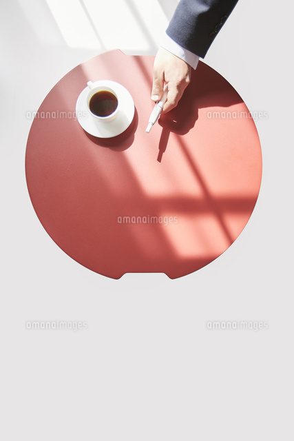 赤い丸テーブルで休憩するアイコスを持つ男性の手元 の写真素材 イラスト素材 アマナイメージズ