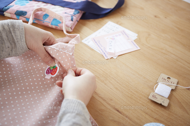 子供のエプロンにアップリケを縫い付ける女性 の写真素材 イラスト素材 アマナイメージズ