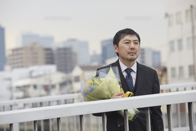 退職をして花束を抱えながら途方に耽る男性社員 の写真素材 イラスト素材 アマナイメージズ