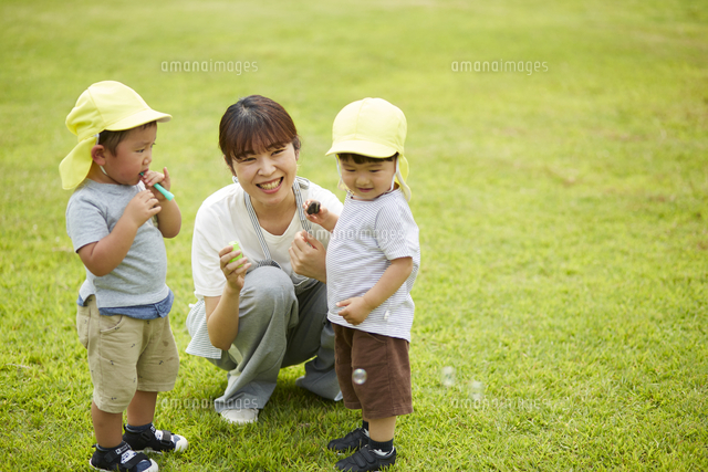 芝生の上でシャボン玉をする子供達と保育士 の写真素材 イラスト素材 アマナイメージズ