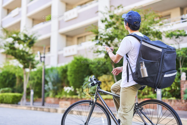 自転車でフードデリバリーをする配達員の後ろ姿 の写真素材 イラスト素材 アマナイメージズ