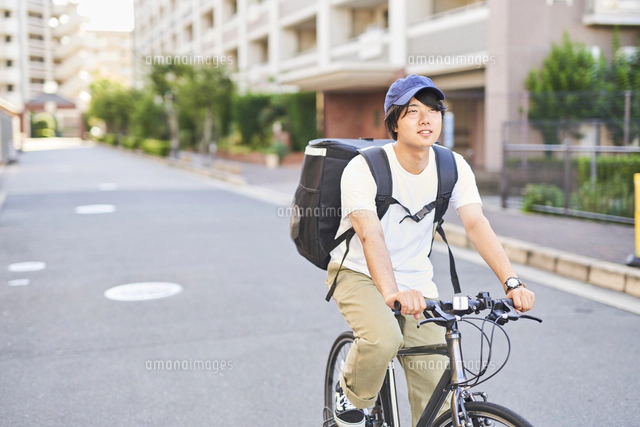 携帯を持ったフードデリバリーの配達員の後ろ姿 の写真素材 イラスト素材 アマナイメージズ