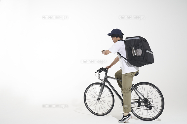 自転車に乗って時計を見るフードデリバリーの配達員と白い背景 の写真素材 イラスト素材 アマナイメージズ