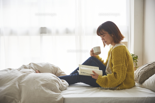 ベッドの上で座って本を読む女性[10179022513]の写真・イラスト素材