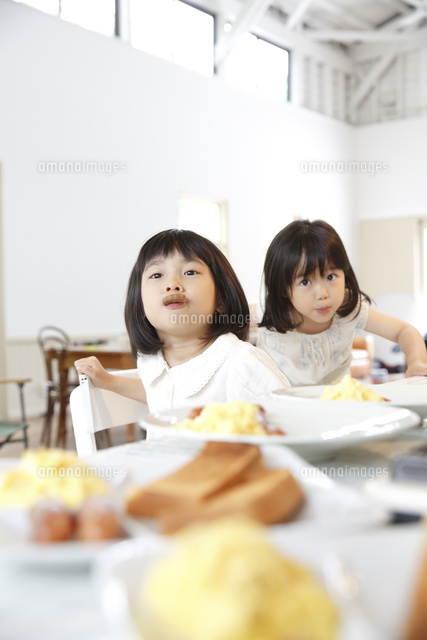 朝食を待ちながらつまみ食いする幼い姉妹 の写真素材 イラスト素材 アマナイメージズ