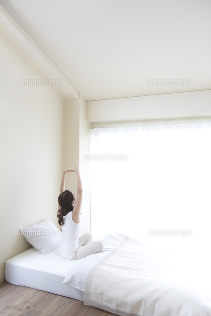 窓際のベッドで伸びをする後姿の若い女性 の写真素材 イラスト素材 アマナイメージズ