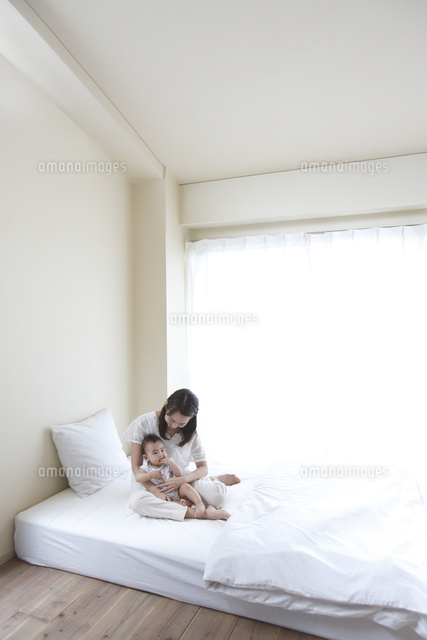 窓際のベッドで赤ちゃんを抱く若い母親 の写真素材 イラスト素材 アマナイメージズ