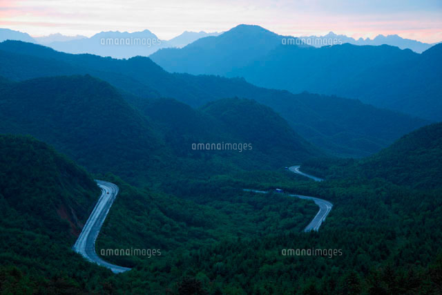 山の曲がりくねった道と夕焼けの空 の写真素材 イラスト素材 アマナイメージズ