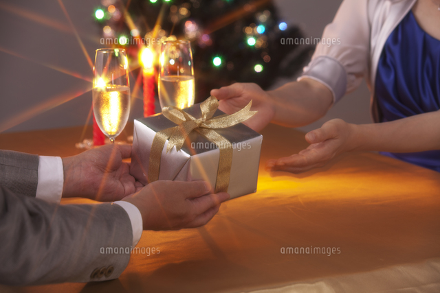クリスマスツリーでプレゼントを渡すカップルの手 の写真素材 イラスト素材 アマナイメージズ