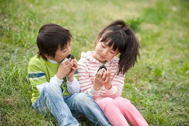 土手の草に座っておにぎりを食べる子供のカップル の写真素材 イラスト素材 アマナイメージズ