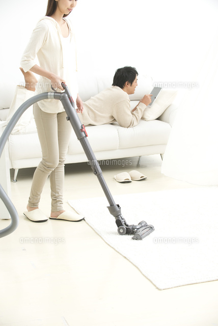 掃除機をかける女性とソファの男性夫婦 の写真素材 イラスト素材 アマナイメージズ
